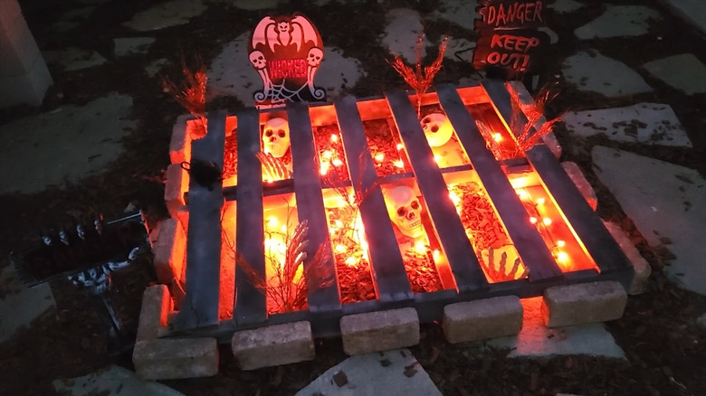 A painted pallet with plastic skeletons inside, seen at night with orange lights illuminating the decoration.
