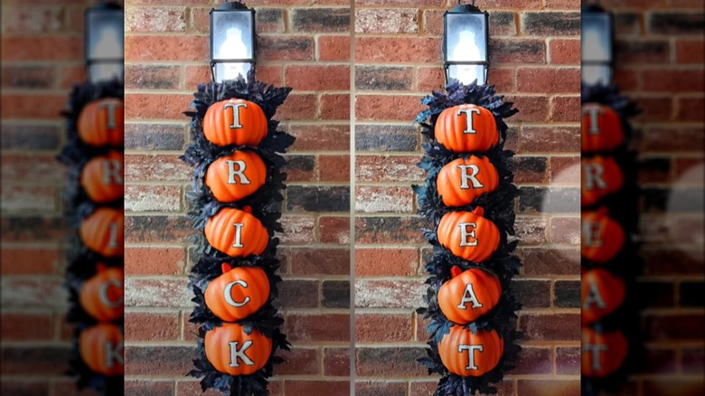 Two of three "trick or treat" signs are hung from lights on a front porch.