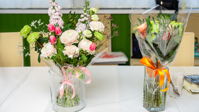 A pair of pretty glass vases sitting on a white counter top and filled with floral bouquets