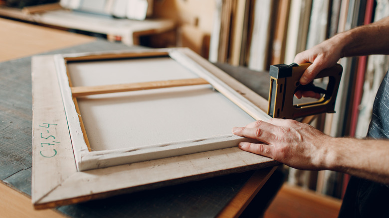 person using staple gun on wood frame for picture