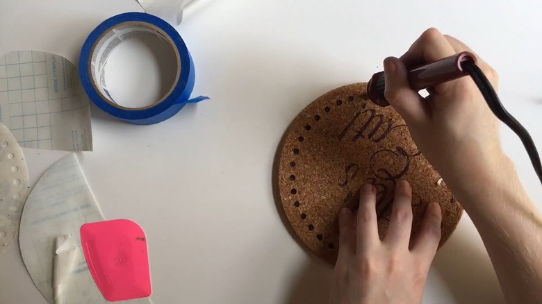 Person decorating cork trivets with wood burner