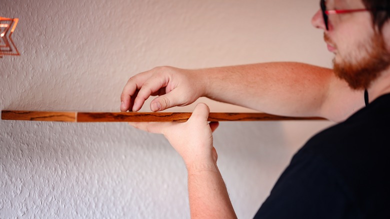 man installing holding DIY wood shelf up to wall