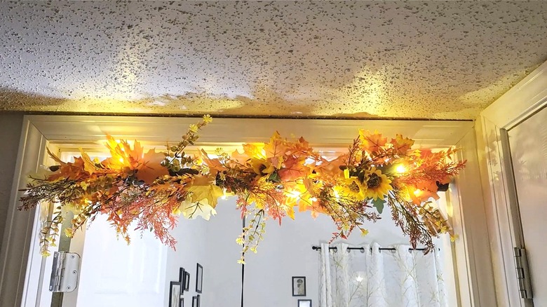 Door decoration made from a tension rod covered in a pool noodle and artificial plants in fall ornaments