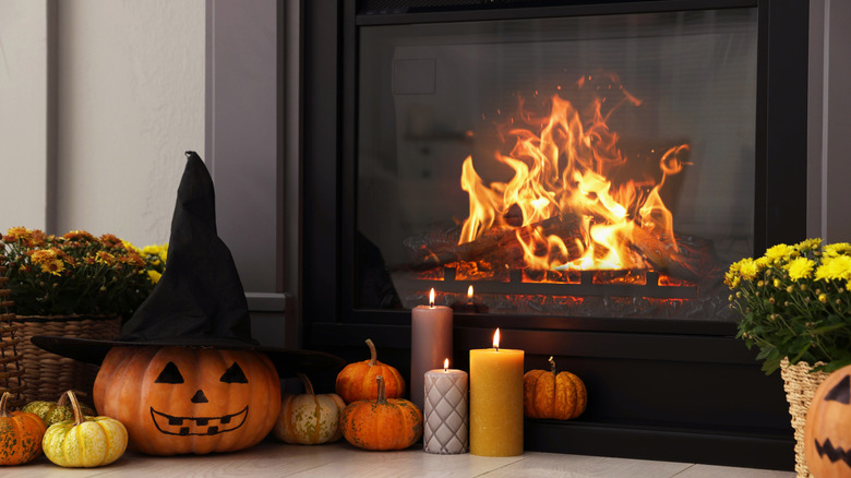 a lit fireplace with Halloween pumpkins, mums, and candles