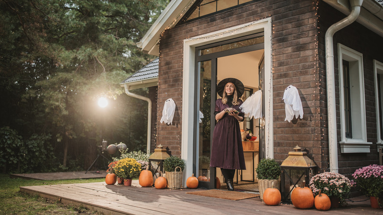 A backyard and patio decorated for Halloween with a woman in a witch's hat standing in the doorway.