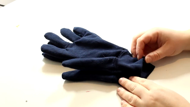 Navy DIY gardening gloves made from an old sweatshirt laying on a white table with a person's hands nearby