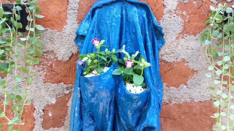 Planter made from an old shirt, hanging on a brick wall with plants in pockets