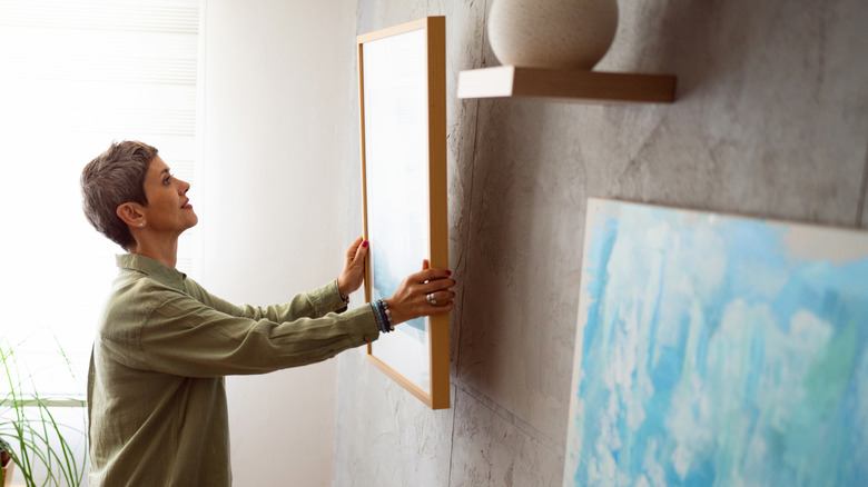 Woman hanging up framed artwork onto a wall