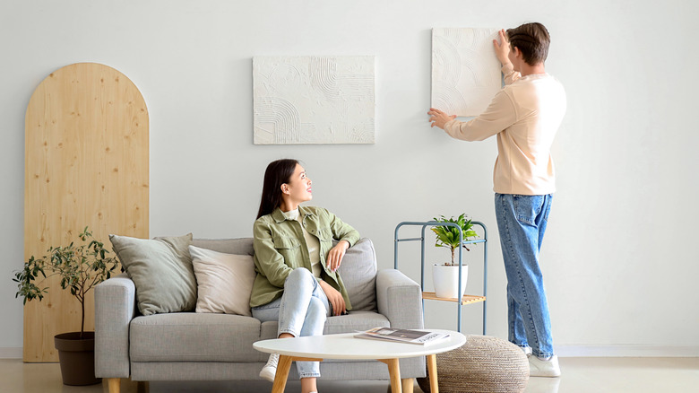 Couple hanging artistic canvas in living room
