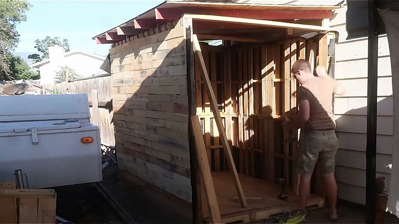 A man works on adding doors to a shed built using wood pallets