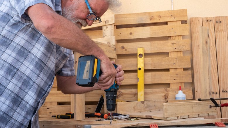 A person works on a project using scrap wood pallets and a drill