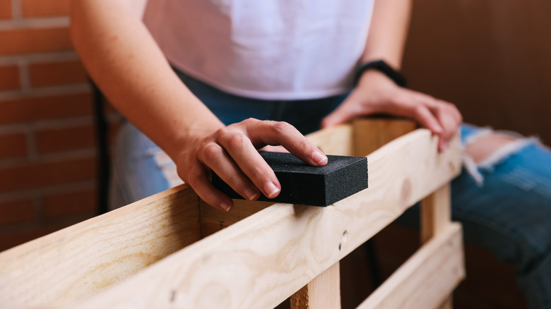 A person sands a wood pallet