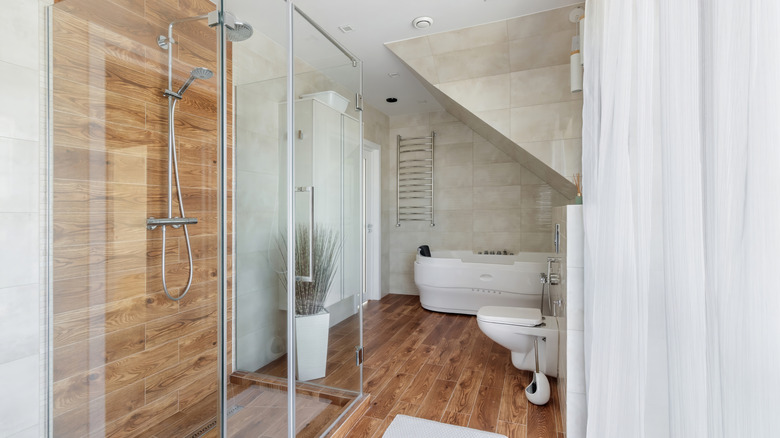 A bathroom with a wooden, or wooden-looking floor and shower wall.