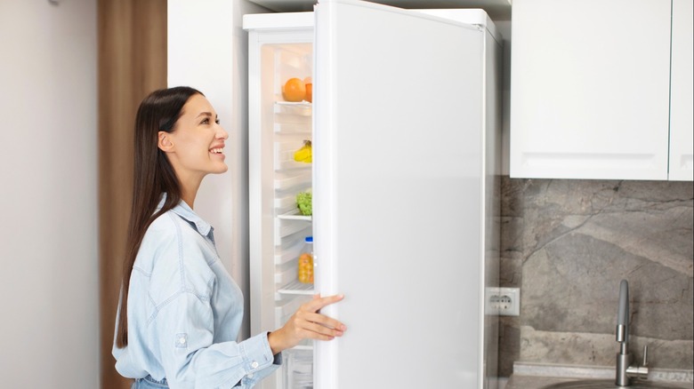 smiling woman looking inside white fridge in kitchen
