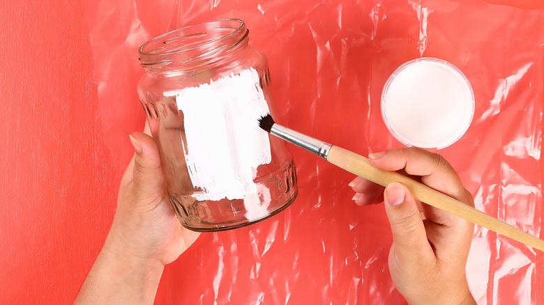 A person painting a mason jar with white paint
