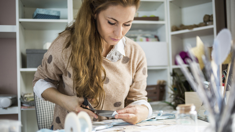 Woman cutting paper at a crafts table.