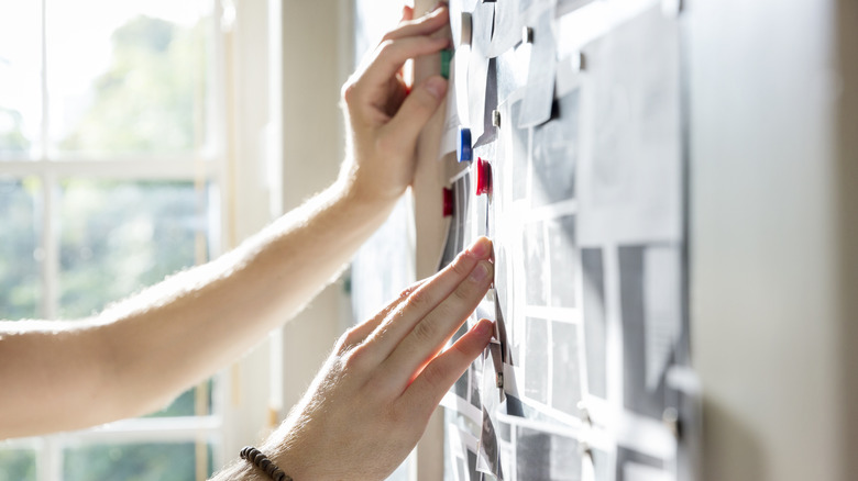 Closeup of a person pinning paper on a board.