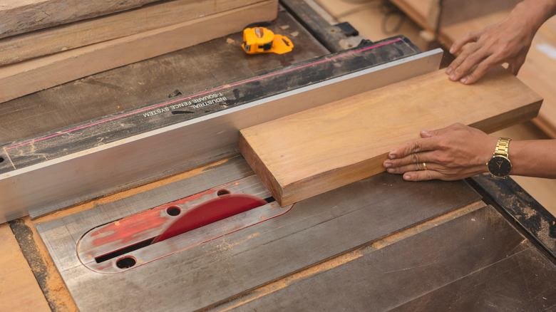 Hands guiding a wooden block through a table saw