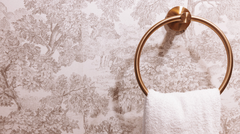 Close-up of a towel ring with white hand towel hanging on it against faded wall paper.