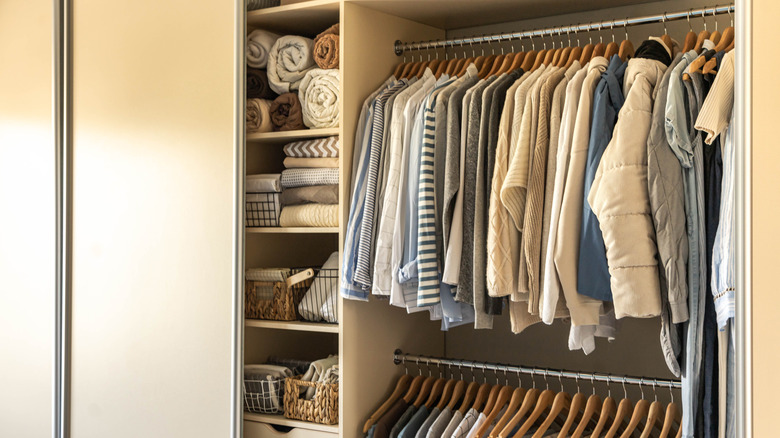 A closet behind a sliding door with two rows of rods to hang clothes, and shelves or blankets and other items