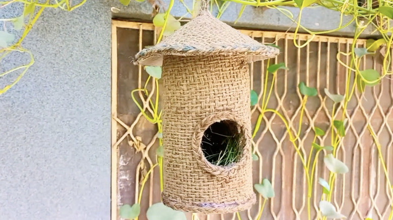 A birdhouse made of a recycled plastic bottle, cardboard, burlap, and twine