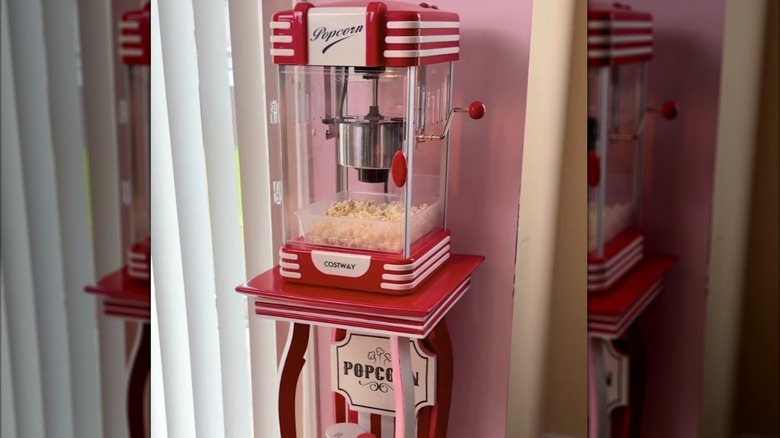 A red-and-white-striped DIY popcorn station made from a vintage side table and a popcorn maker.