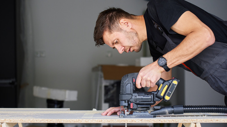 A man using a jigsaw to cut a wooden board