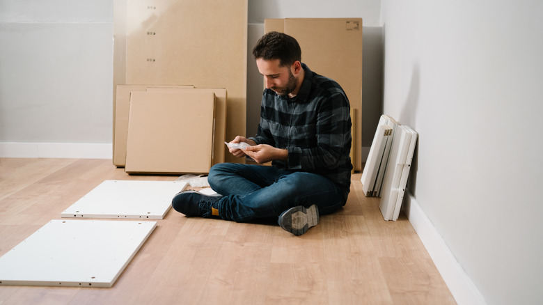 A man reads directions to assemble white furniture from boxes