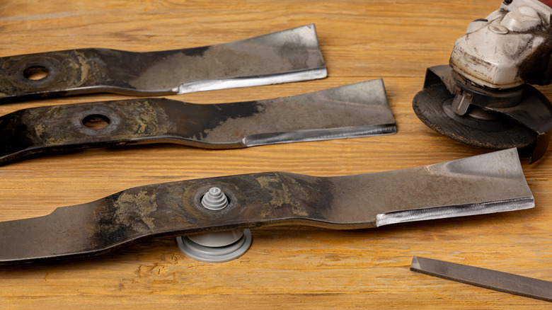 Three lawn mower blades and sharpening tools sitting on a wooden surface