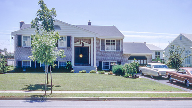 A 1960s style suburban home with brick exterior and two cars in the driveway