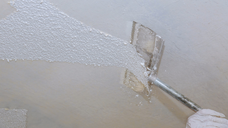 A person uses a metal tool to remove a popcorn ceiling finish