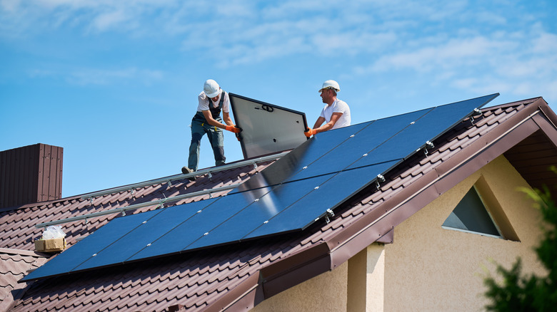 Workers placing solar panels on roof of house