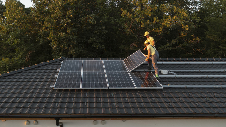 Two installers in hats installing a series of solar panels on a roof