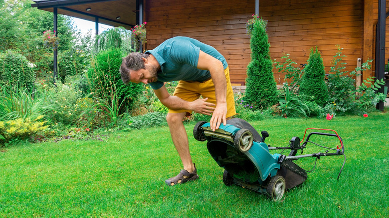 Person lifting lower to look at blade in yard