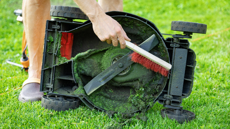 man with brush cleaning lawnmower from old grass
