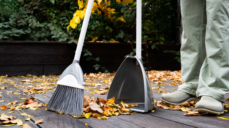 Person in green pants using a broom and dustpan to clean leaves from a deck