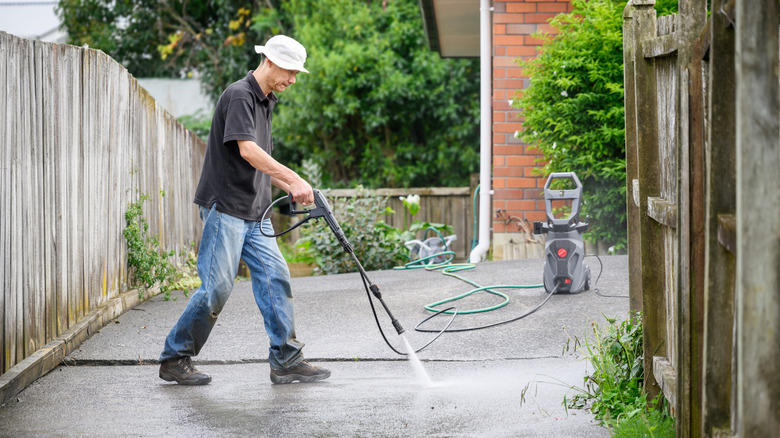 a person wearing protective gear pressure washes a driveway
