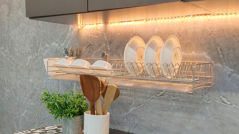 A wall-mounted metal dish rack with white dishes under kitchen cabinet
