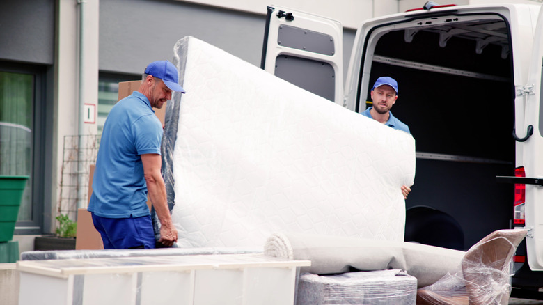 Two men removing a mattress from a van.