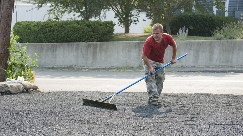 Man using tool to smooth a gravel driveway