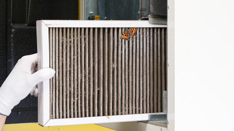 White gloved hand pulling out dirty HVAC filter