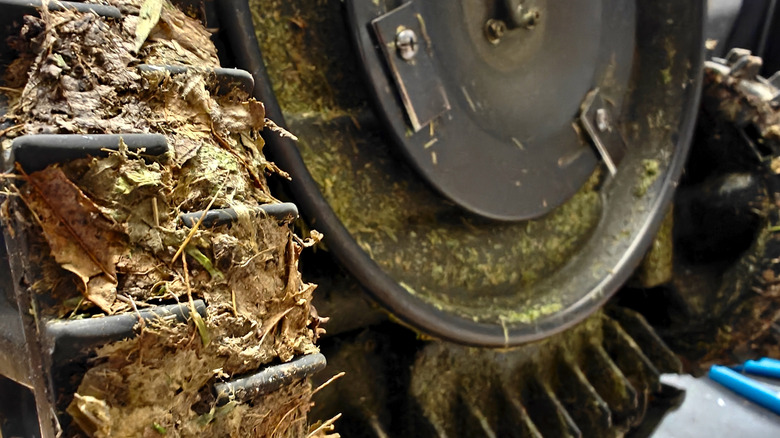 Grass, dirt, and debris clogged wheel of a lawn mower