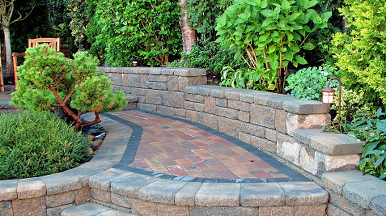 a hardscaped yard with shrubs, a retaining wall, and a brick walkway