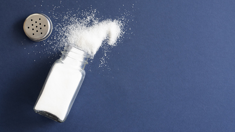 An open salt shaker on a blue counter.