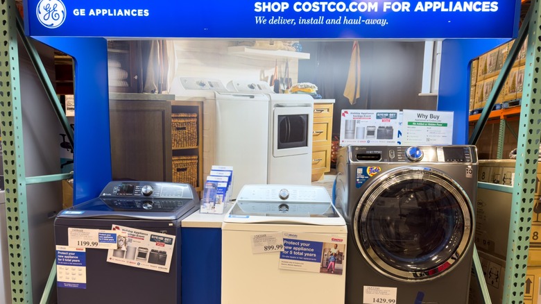 A selection of washing machines available for sale at Costco, beneath a banner that talks about their delivery service.