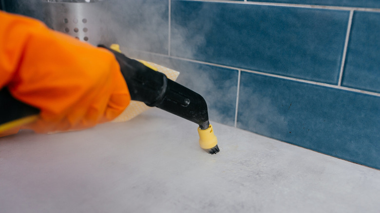 Women cleans bathroom tile with a steam cleaner.