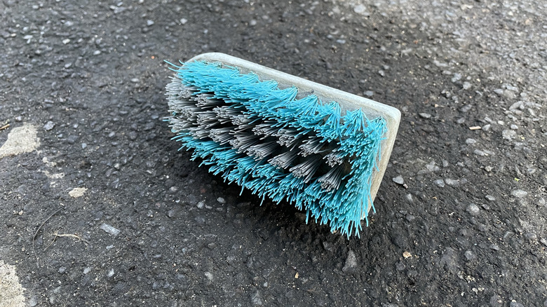 a teal and gray scrub brush on asphalt