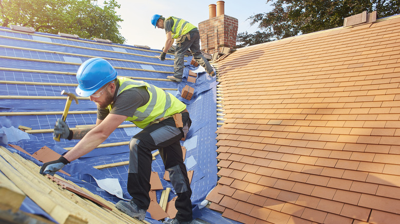 Workers replacing a roof with orange shingles