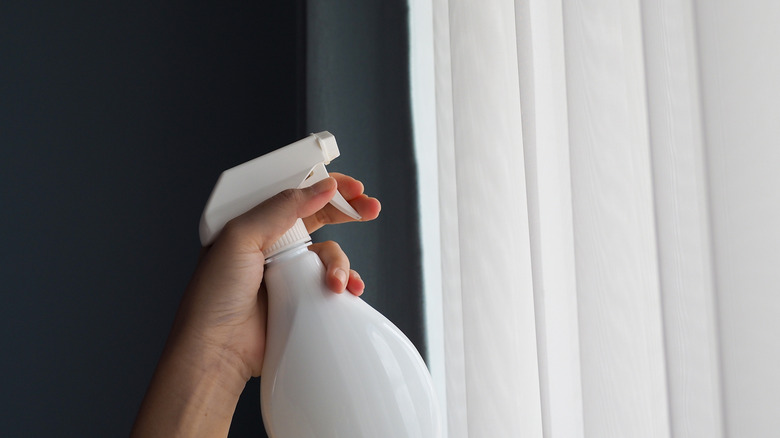 hand holding a spray bottle towards white curtains