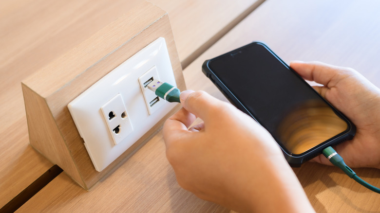 A person using a USB outlet to plug in their phone to charge with a green cable